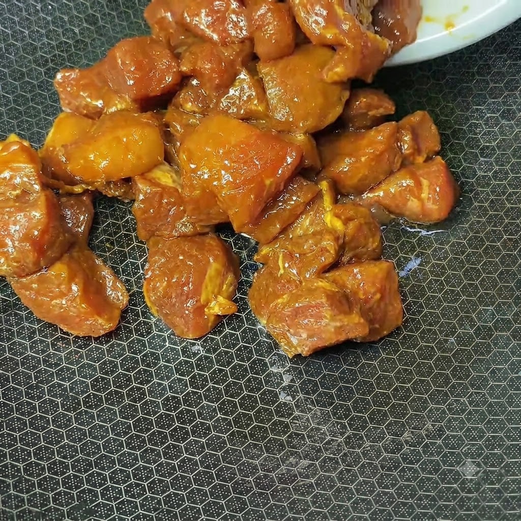 Marinated reddish-brown pork cubes cooking in a hot textured wok.