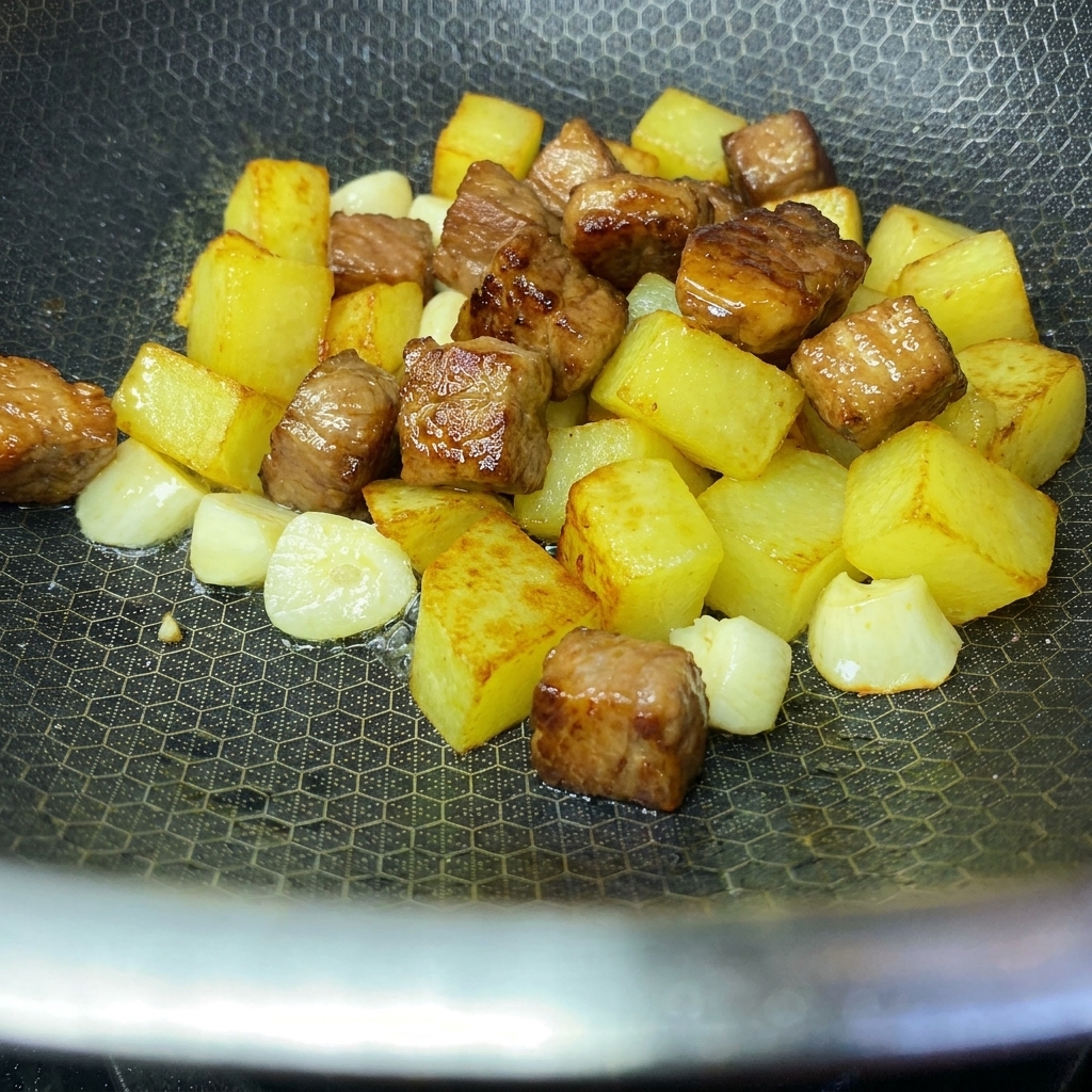 Golden crispy potato cubes and seared pork cubes combined together in a wok.