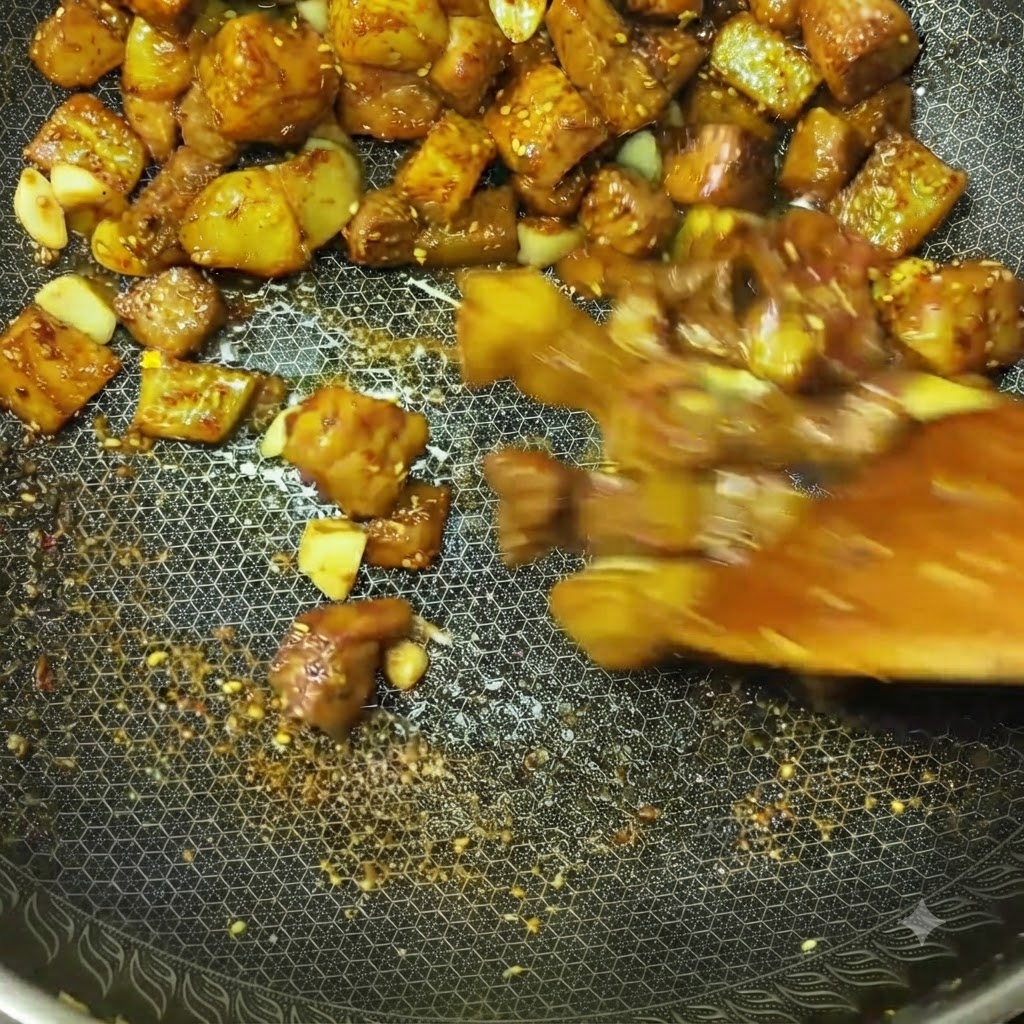 Meat cubes and potato pieces being rapidly stir-fried in a wok with visible spices and seasonings.