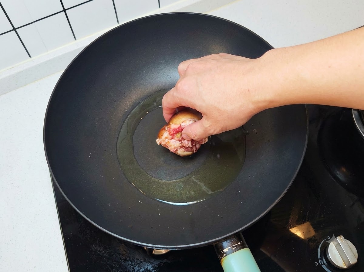 A stuffed mushroom being placed meat-side down into a hot oiled wok.