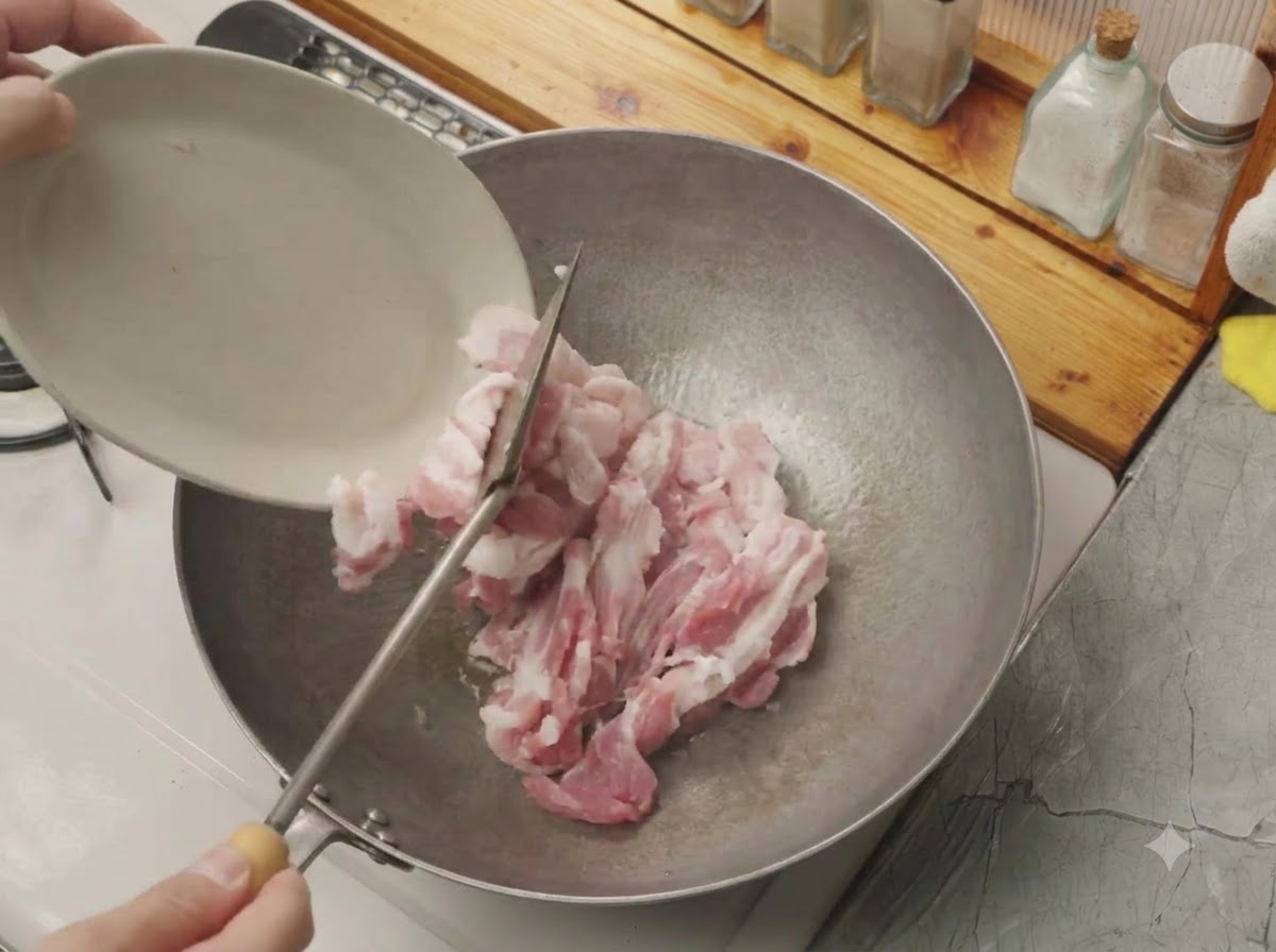 Sliced raw pork belly being tipped from a small white plate into a hot wok.