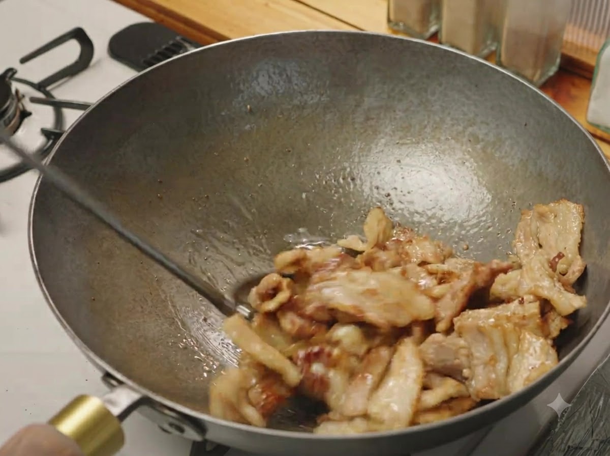 Pork belly slices being stir-fried in a wok until lightly browned and sizzling.
