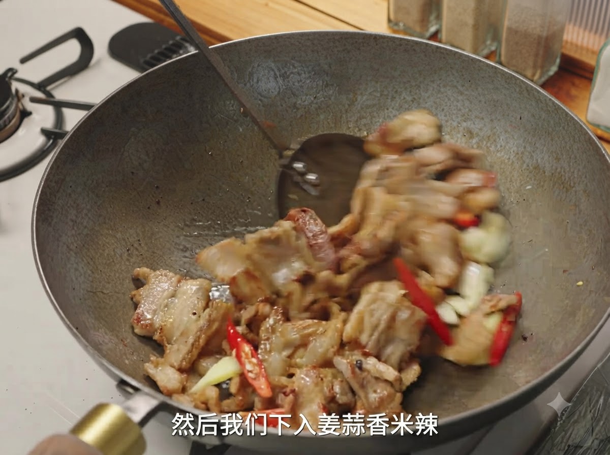 Ginger, garlic, and red chilies being tossed with browned pork pieces in a wok.