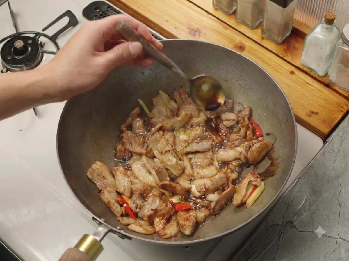 Soy sauce being poured from a spoon onto the hot edge of a wok containing meat and aromatics.