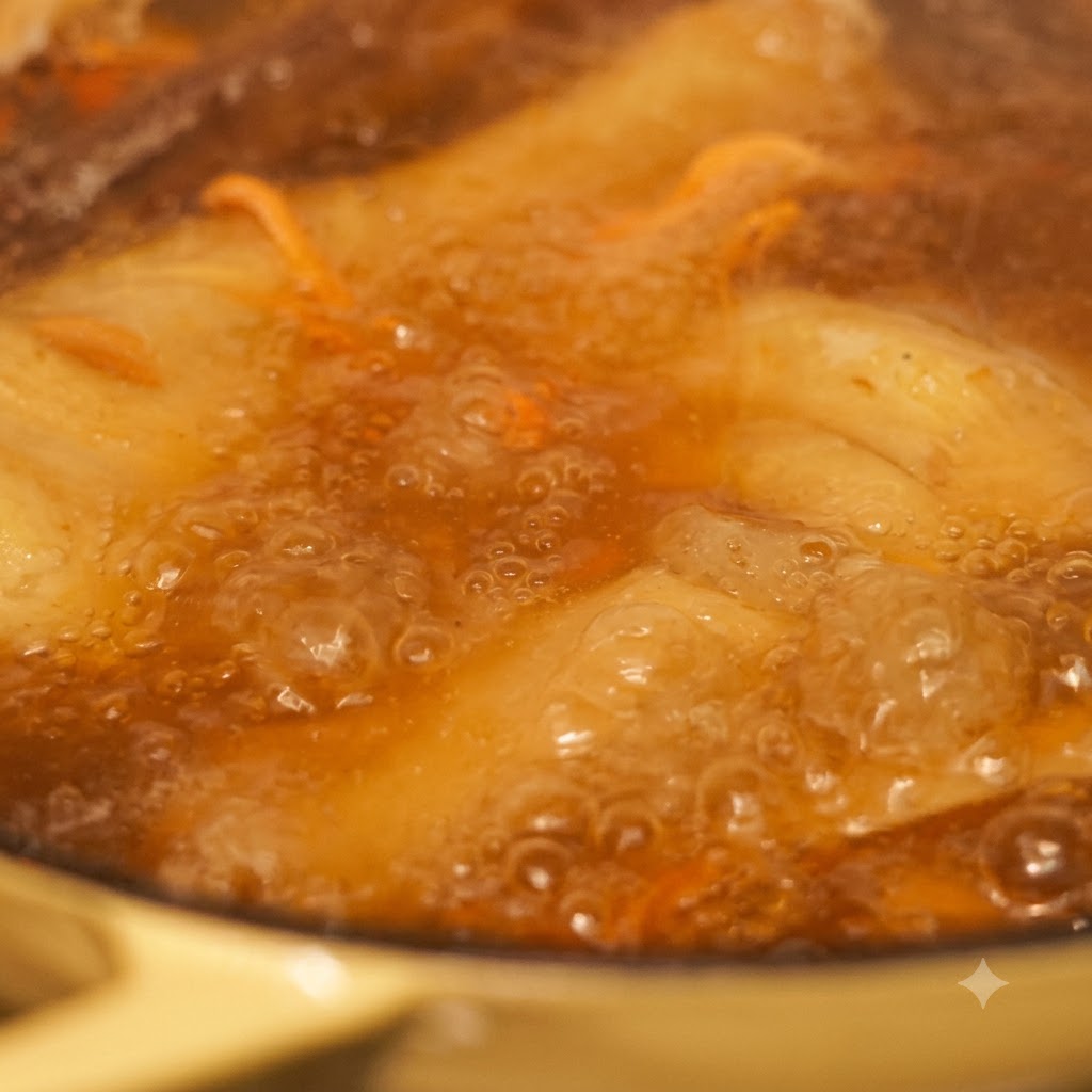 Close-up of noodles and vegetables cooking in bubbling broth.