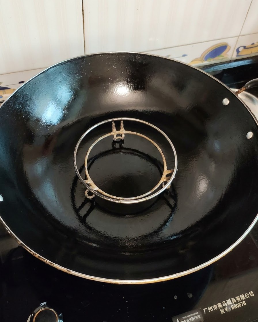 An empty steamer rack set inside a large black wok ready for cooking.