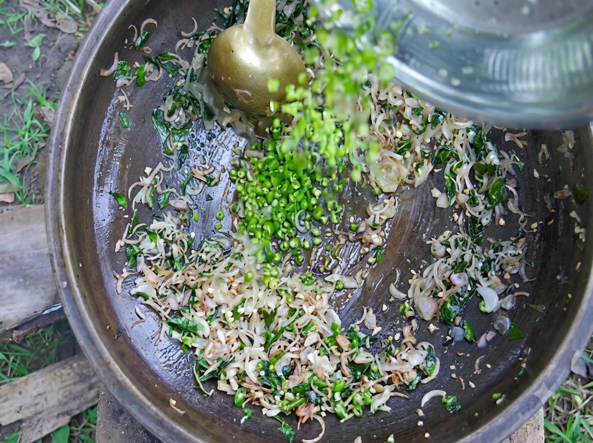 Chopped green chilies and tomatoes being added to the simmering onion and spice mixture in a large iron cooking pot.