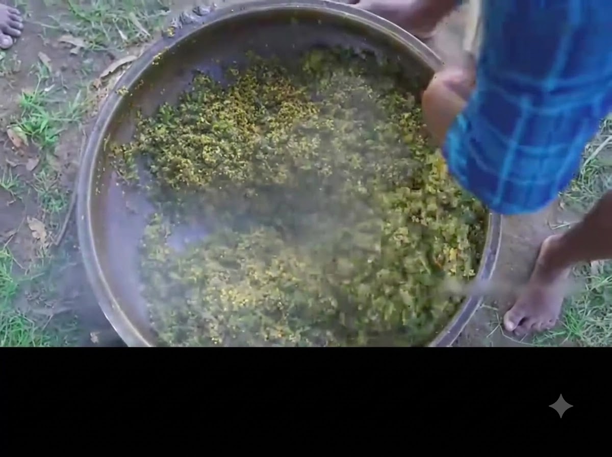 A person stirring the finished green okra and egg curry in a large iron pot.