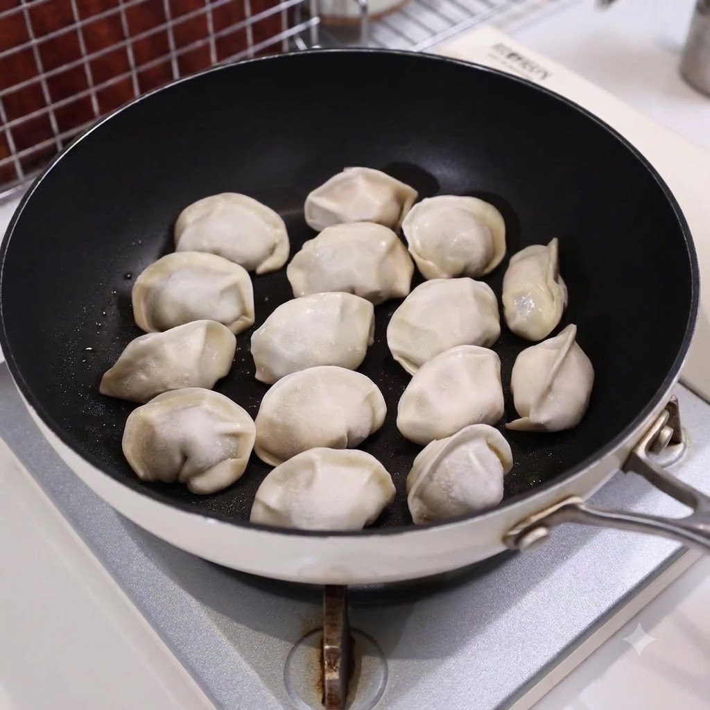 A frying pan filled with arranged dumplings partially submerged in water on a stovetop.