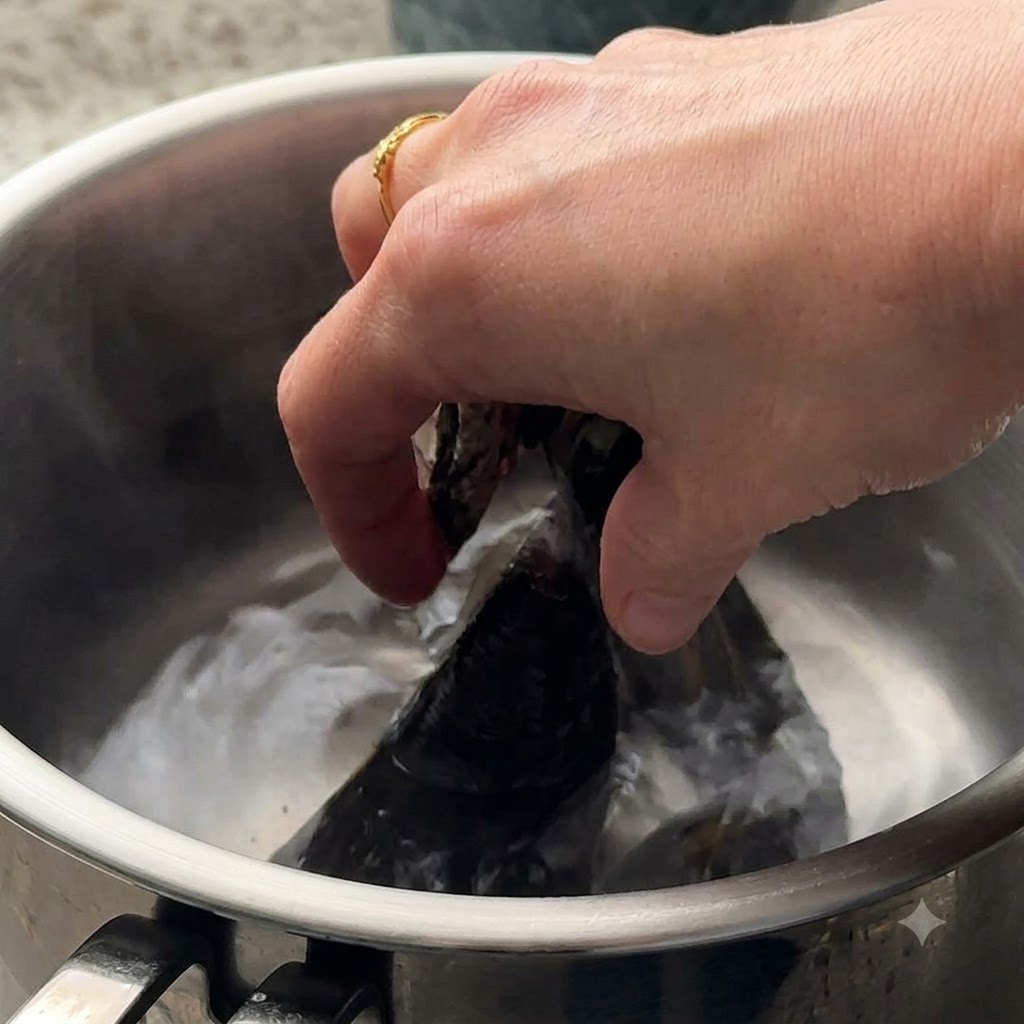 Clams and green mussels being placed into boiling water in a pot.