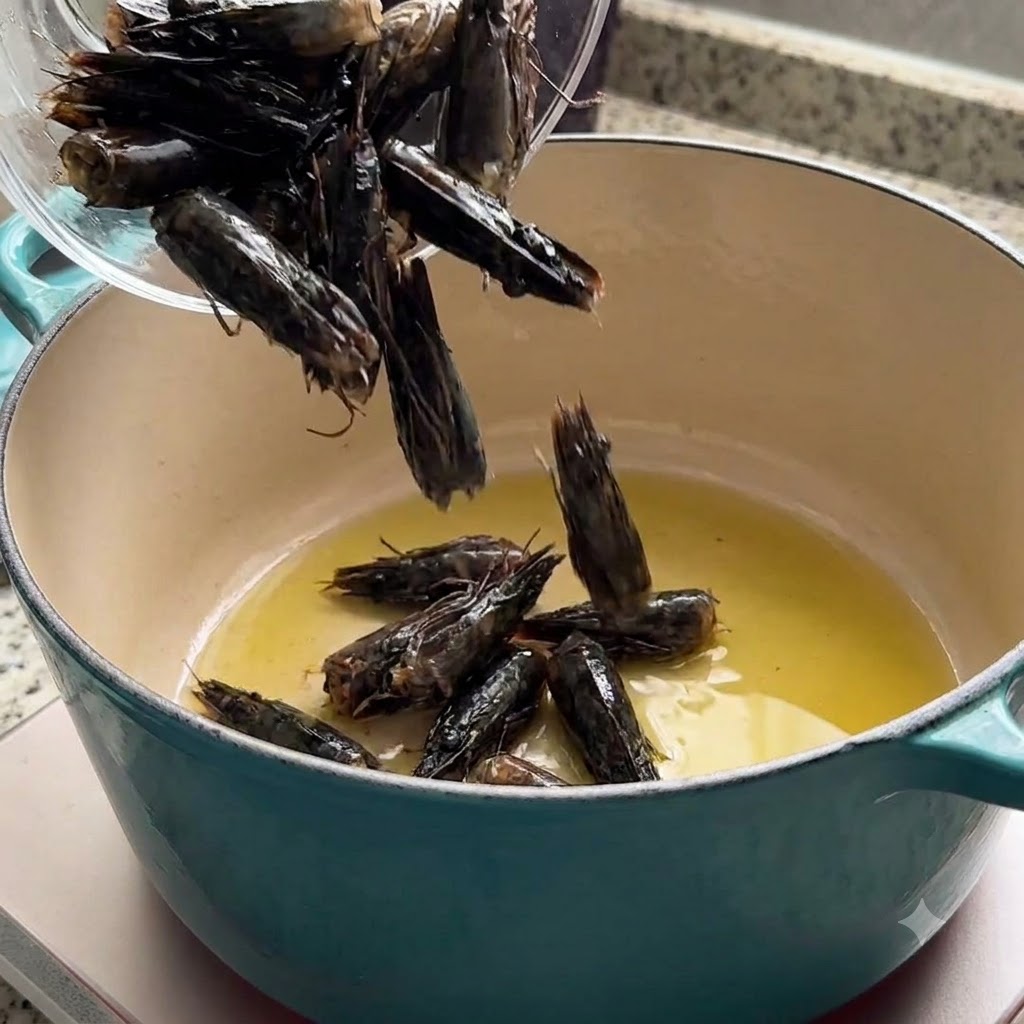 Shrimp heads being poured into a pot with hot olive oil to extract flavor.