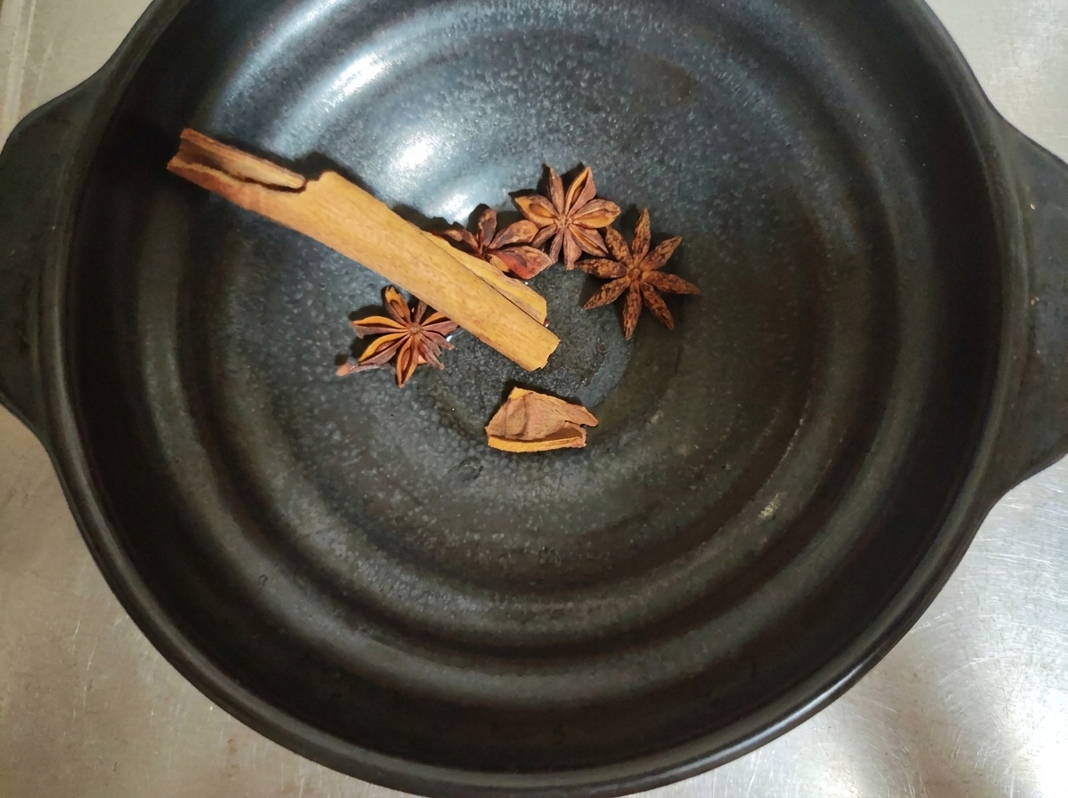 Whole spices like star anise and cinnamon bark inside a dark bowl.