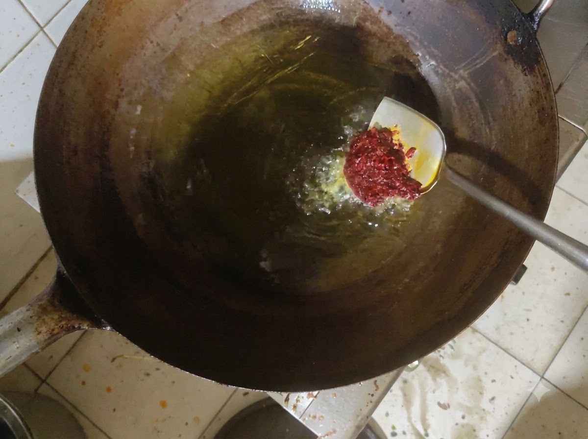 Doubanjiang paste being stirred into hot oil in a wok.