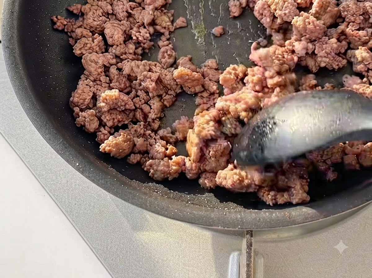 Minced beef being stir-fried with a spatula in a black skillet until lightly browned.