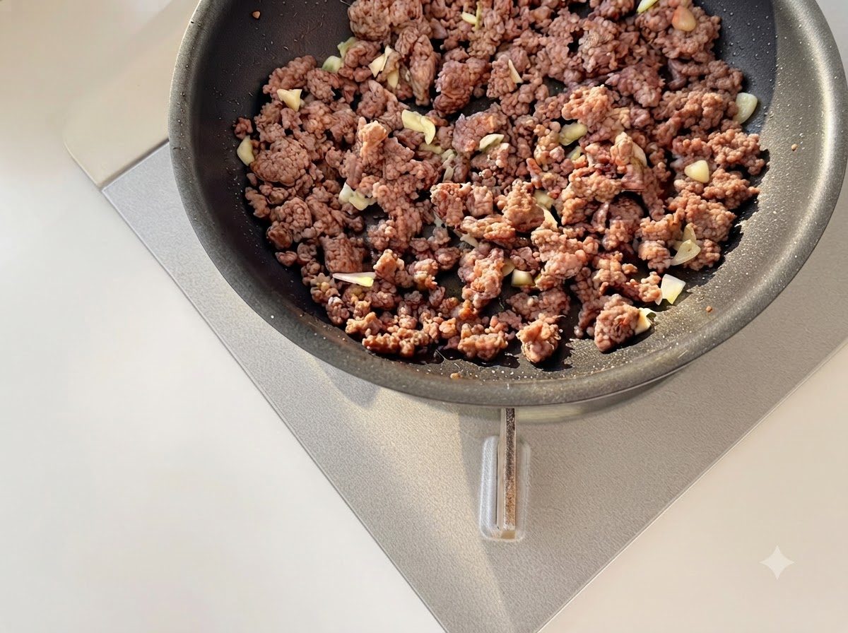 Minced garlic and diced tomatoes being stir-fried together with browned minced beef in a frying pan.