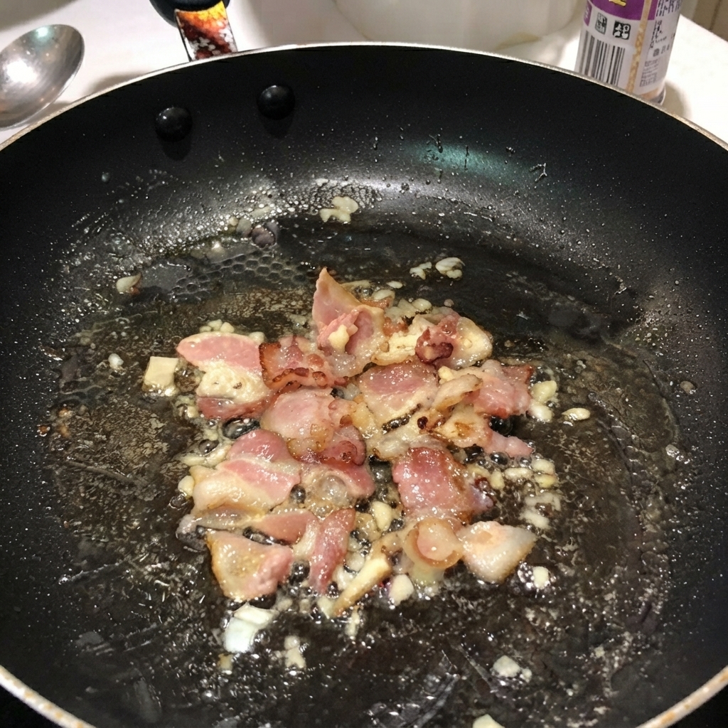 Boiled penne pasta mixed with bacon and onions inside a black frying pan.