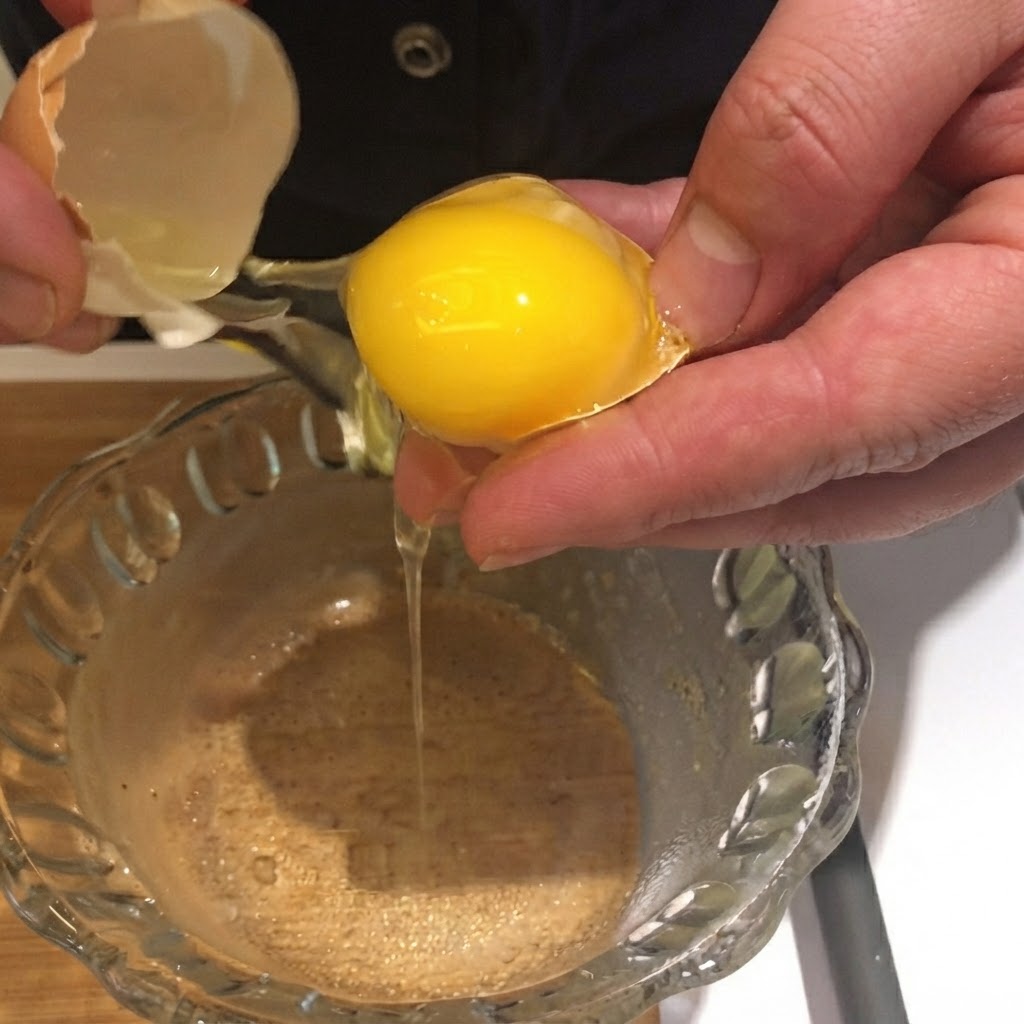 An egg yolk being cracked and dropped from its shell into a clear glass bowl.