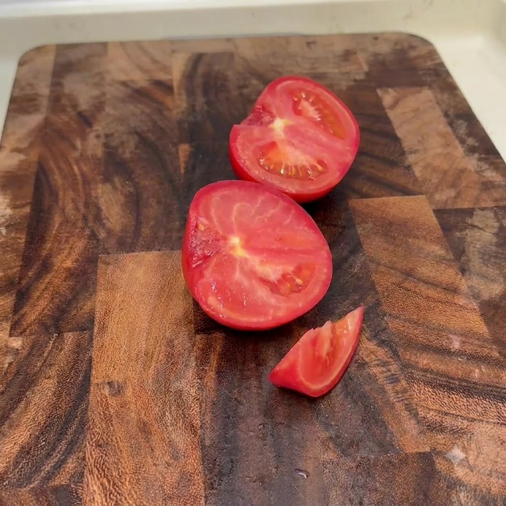 Fresh tomatoes cut into halves and small chunks on a wooden cutting board.