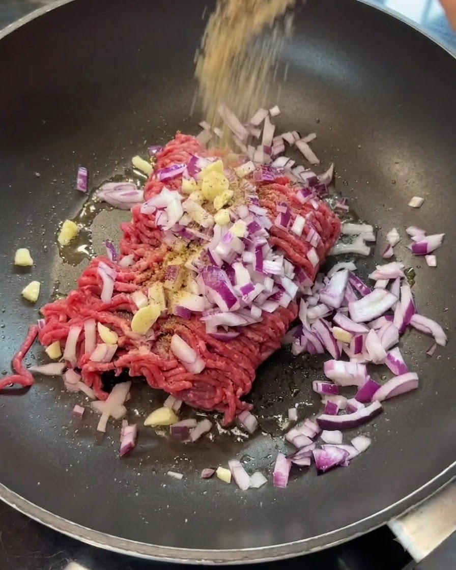Spices being poured over ground beef and onions in a frying pan.