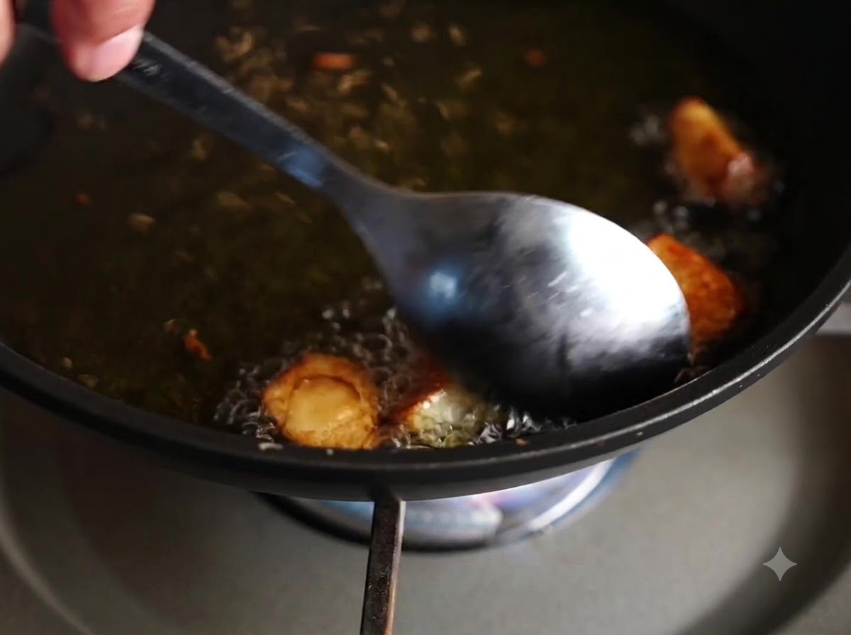 A spoon stirring and turning garlic cloves frying in hot oil.