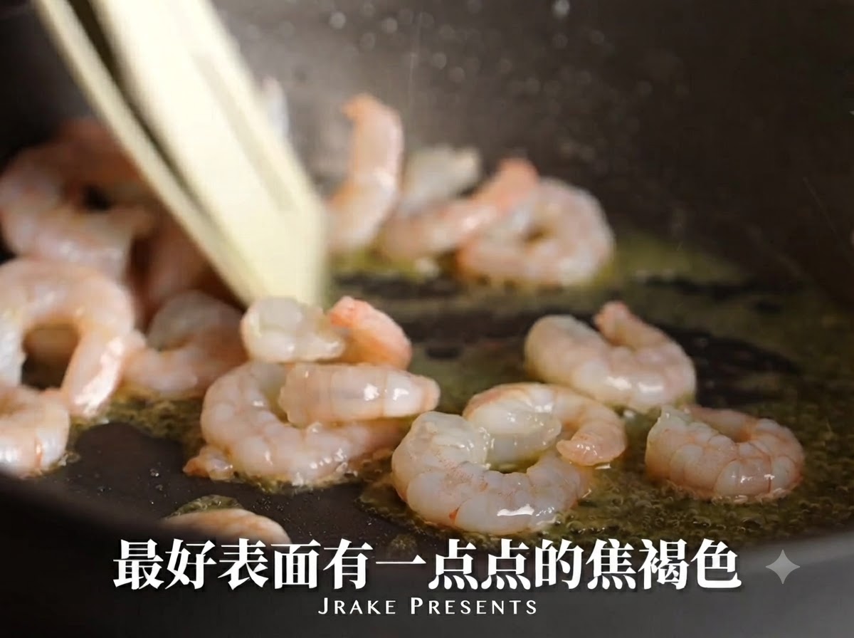 Shrimp searing in a pan with oil, turning pink and developing a caramelized surface.