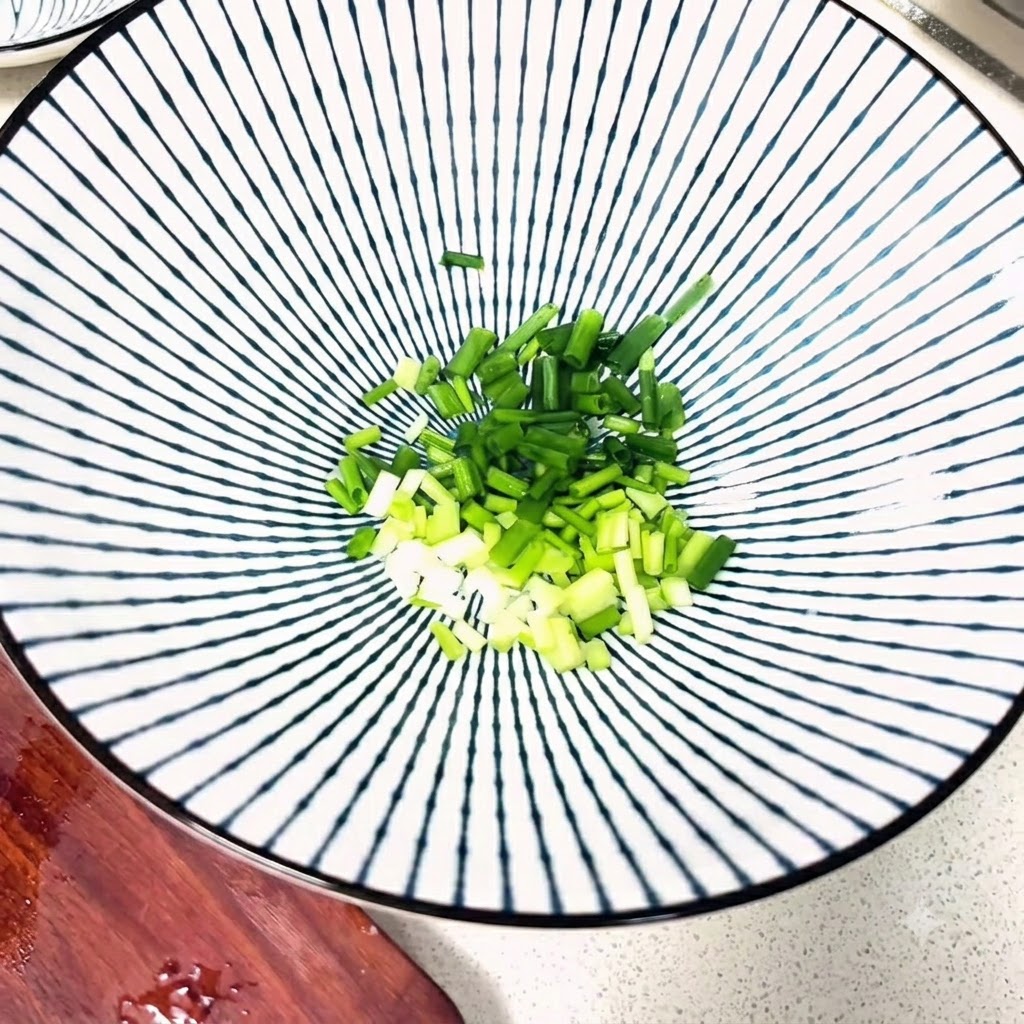 Chopped green onions and various seasonings arranged inside a patterned ceramic bowl.