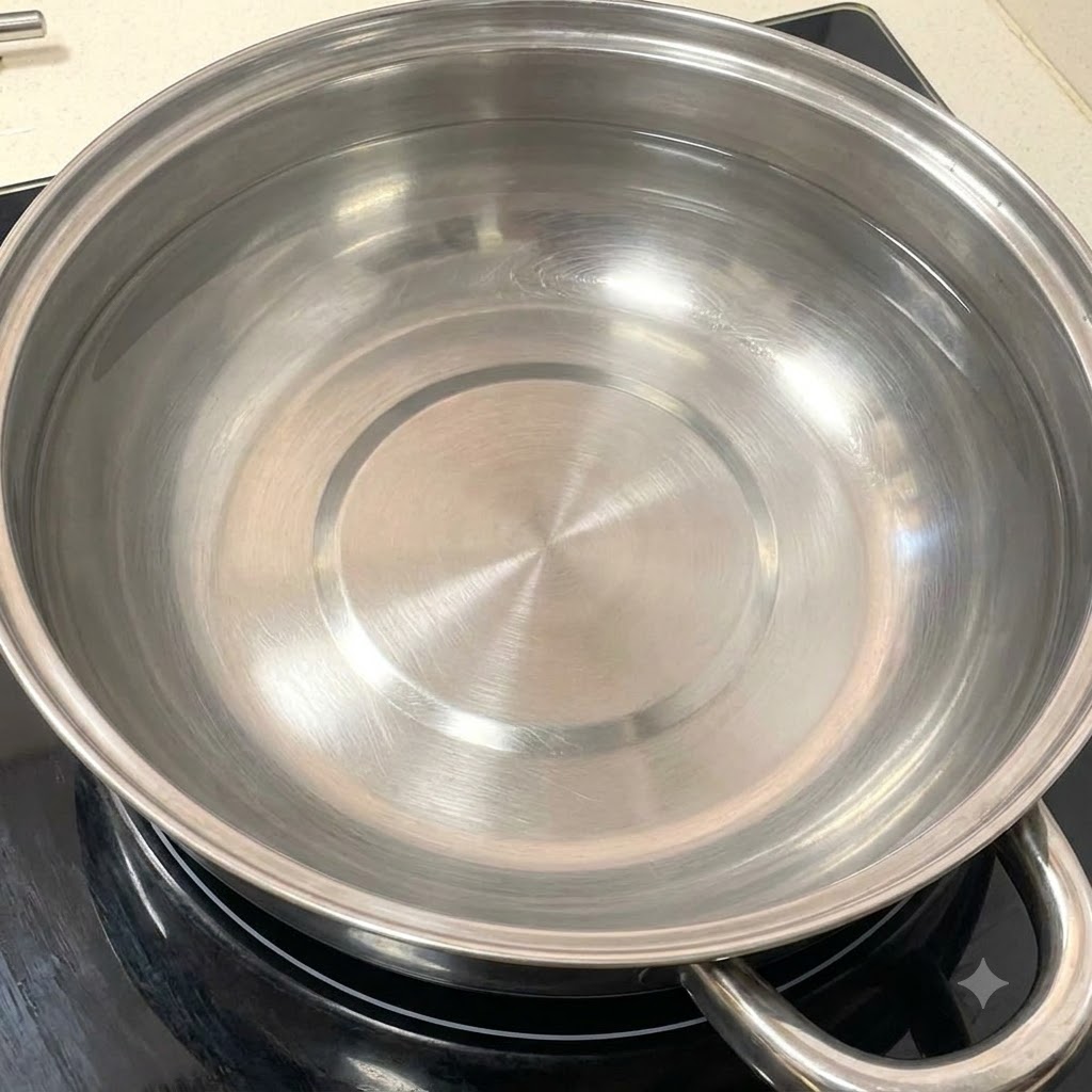A clean stainless steel pot filled with water resting on a stovetop burner.