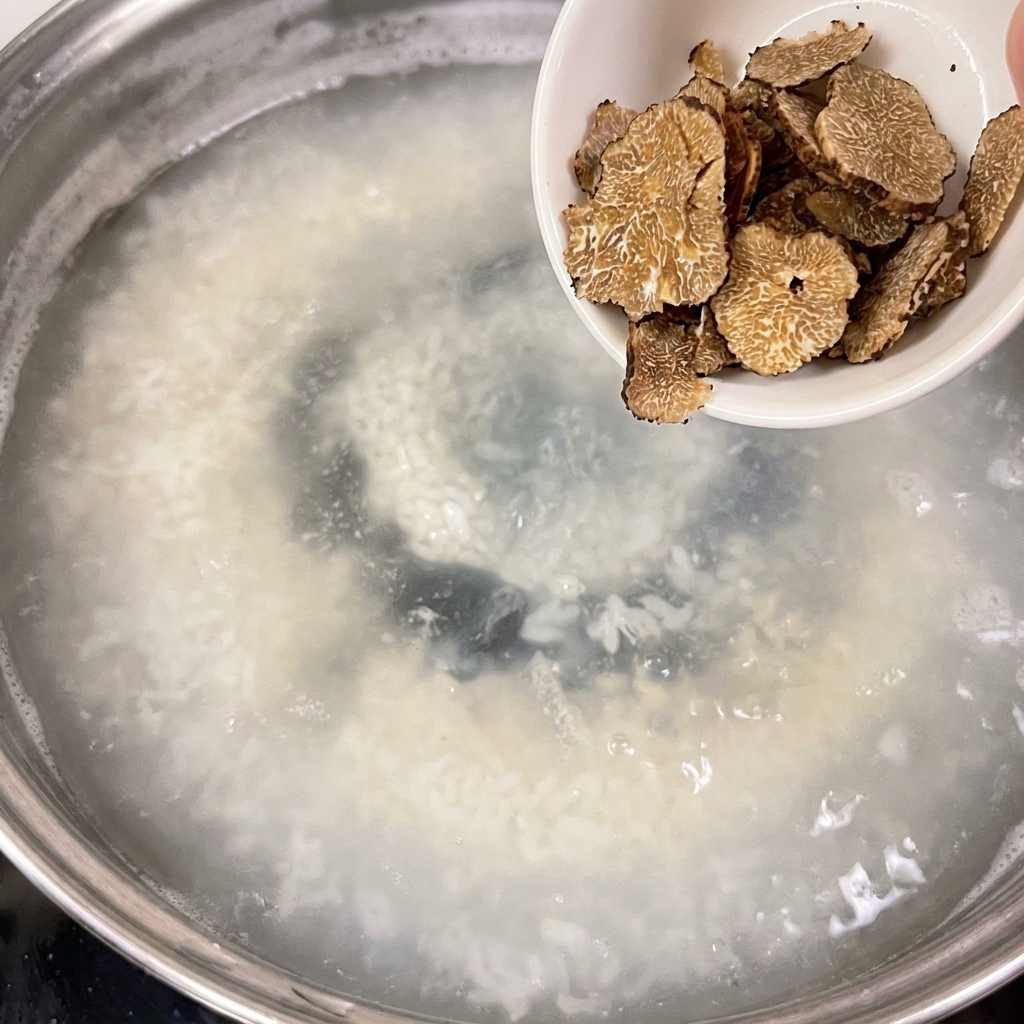 A small white bowl containing sliced truffles being poured into a pot of simmering water.