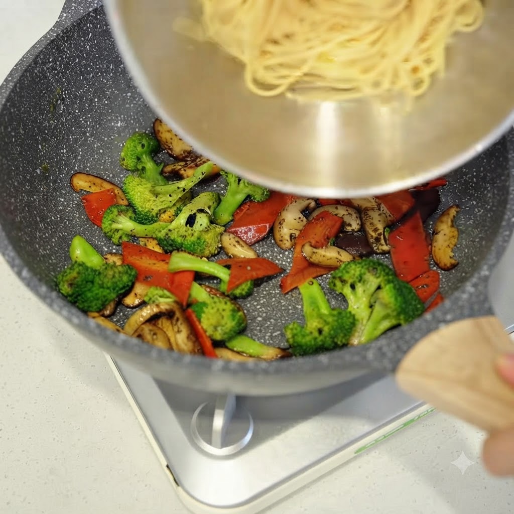 Cooked spaghetti being added from a bowl into the pan with stir-fried vegetables.