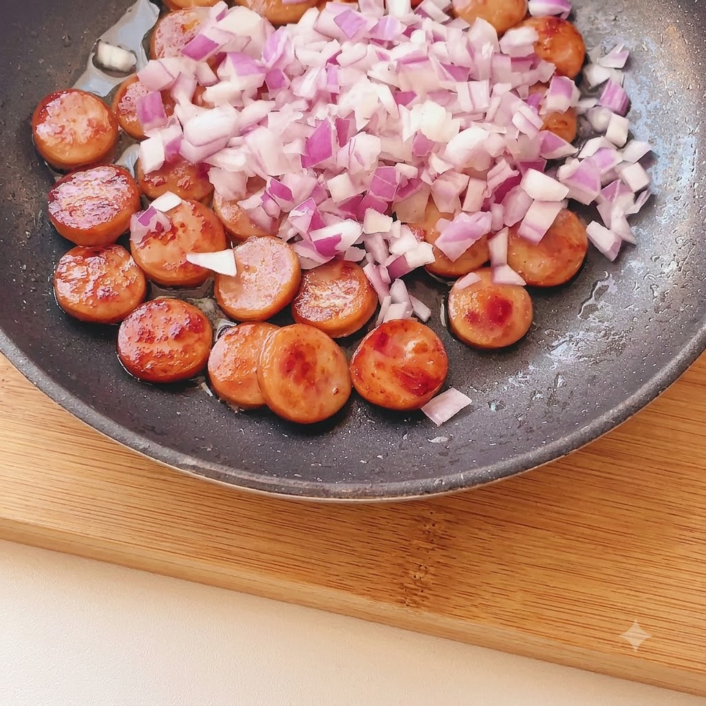 Finely diced red onion scattered over browned sausage pieces in a frying pan.