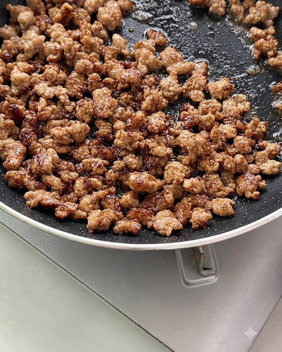 Ground meat mixed with chopped green onions and garlic sizzling in a pan.