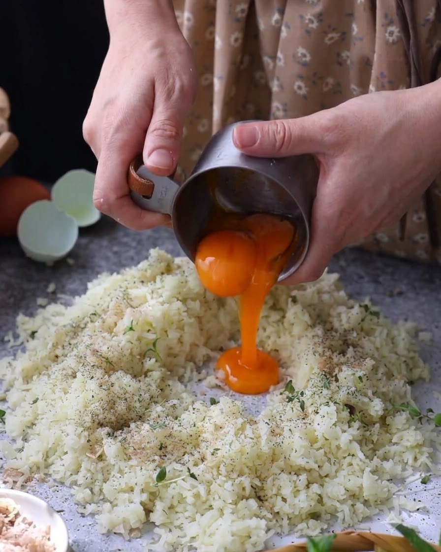 Raw egg yolks being poured into the center of seasoned mashed potatoes.