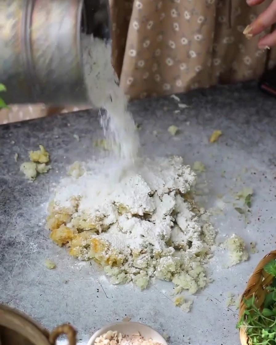 Flour being poured from a container onto the potato and egg mixture on the table.