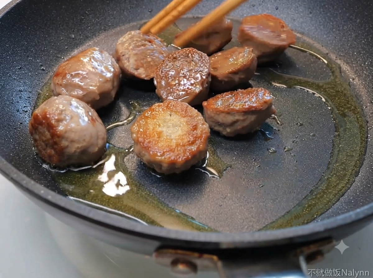 Beef ball halves sizzling in a frying pan with oil, being moved by wooden chopsticks.