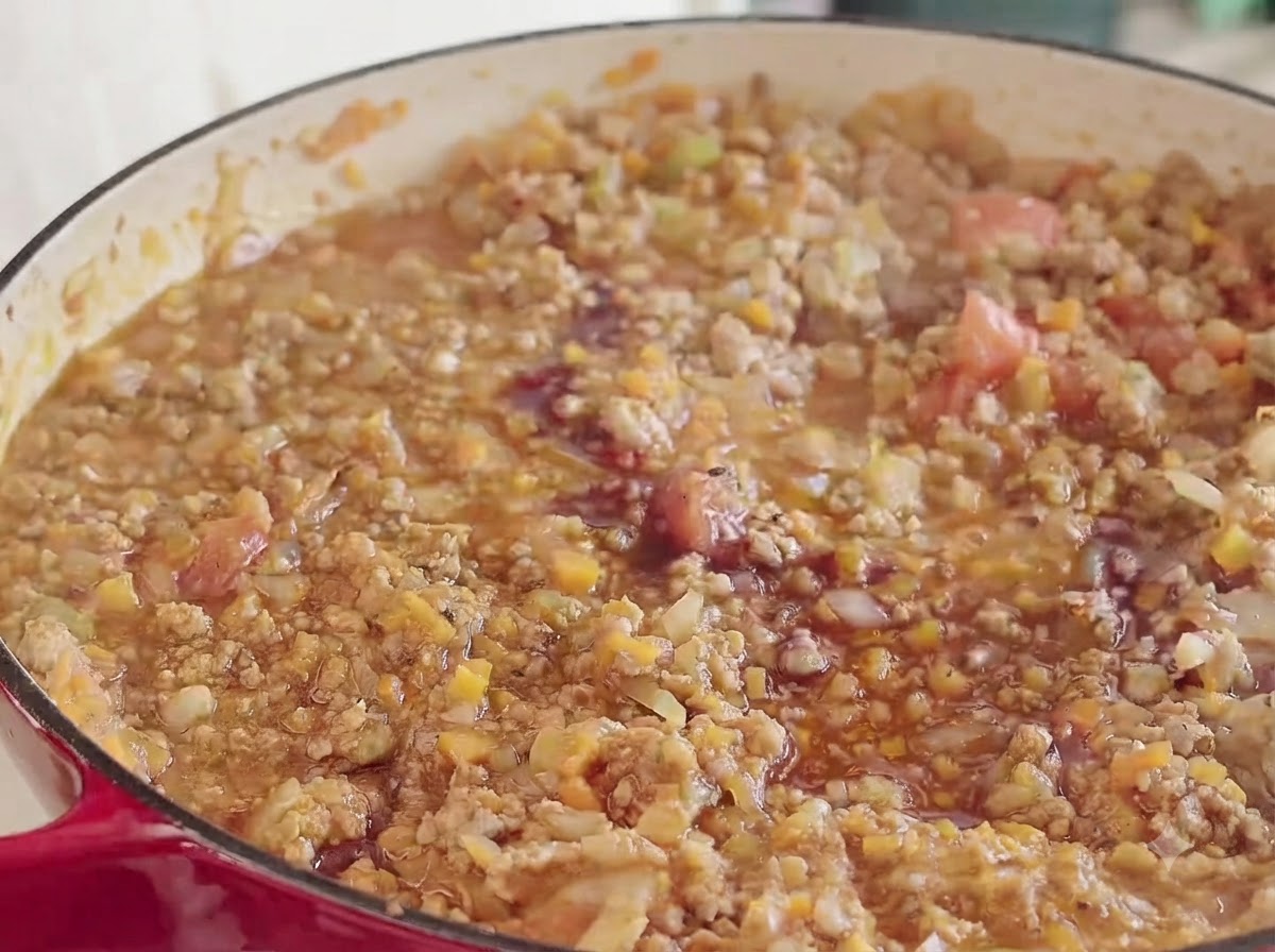 A splash of red wine being poured into the simmering meat and vegetable mixture inside a red pot.