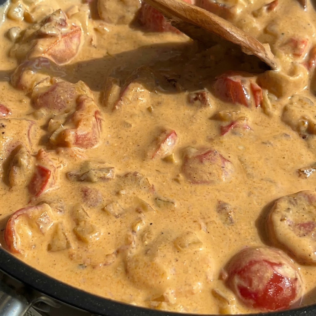 Cooked pasta, spinach, and salmon mixed into a thick creamy sauce inside a frying pan.