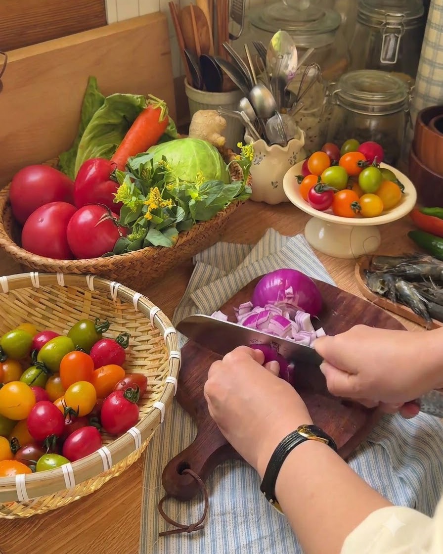 A hand using a knife to cut cherry tomatoes into halves on a wooden cutting board.