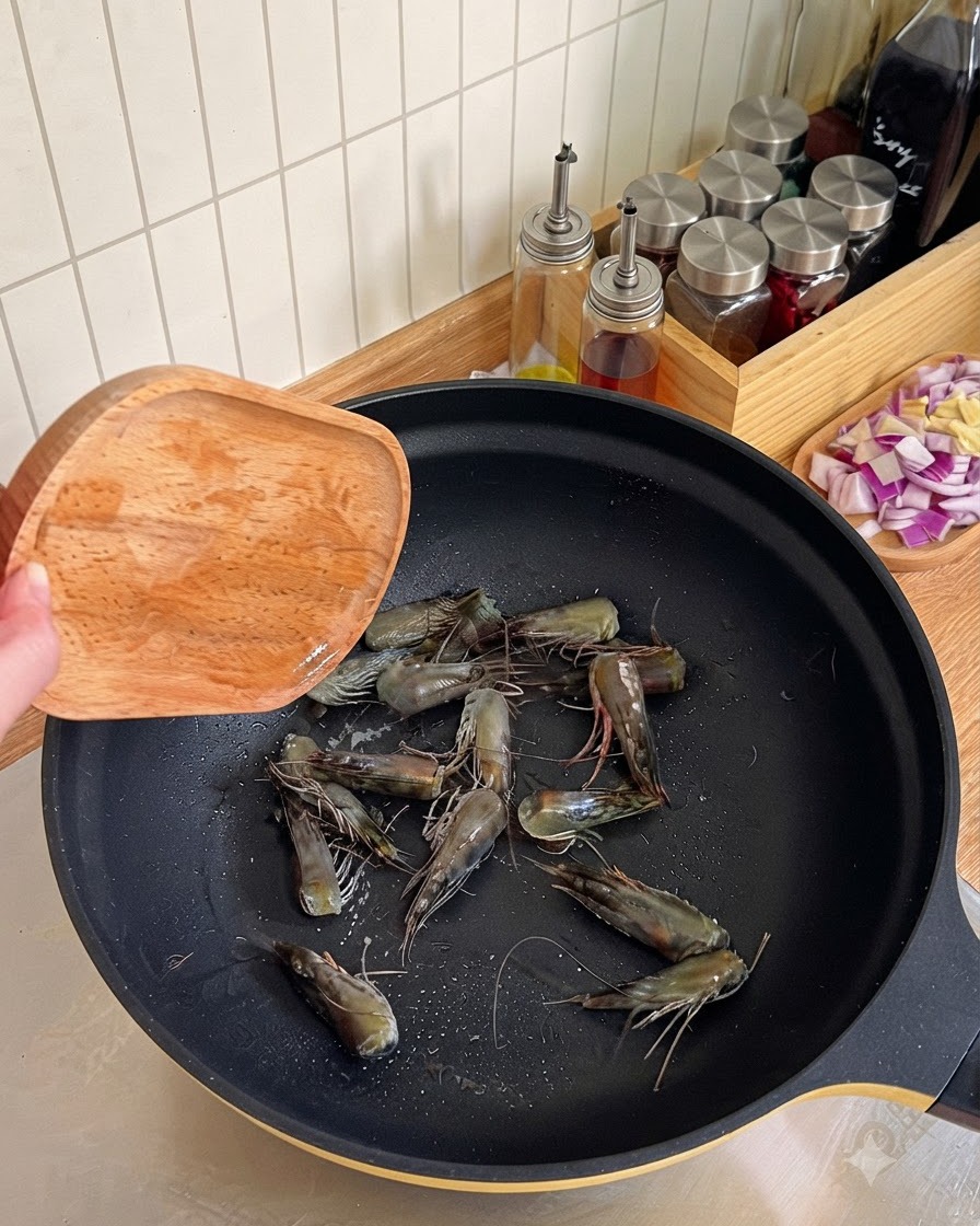Shrimp heads being fried and pressed with a wooden spatula in a black wok to render oil.