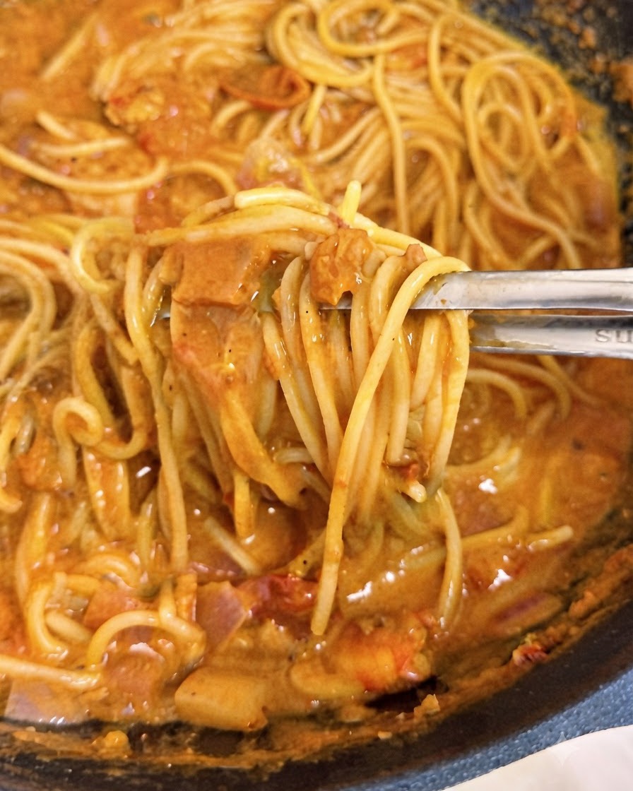 Tongs lifting strands of spaghetti coated in creamy pink tomato sauce inside a wok.