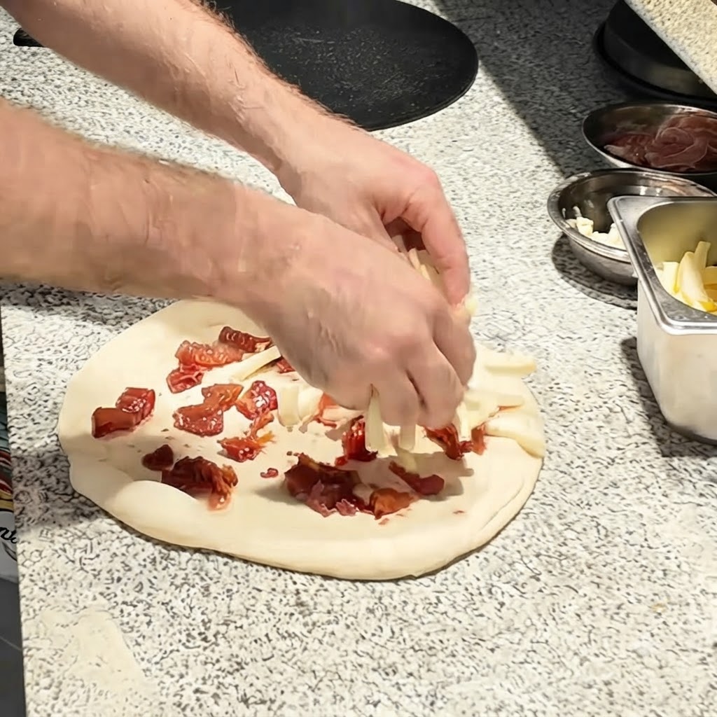 Mozzarella cheese strips being sprinkled over the tomato base on the pizza dough.