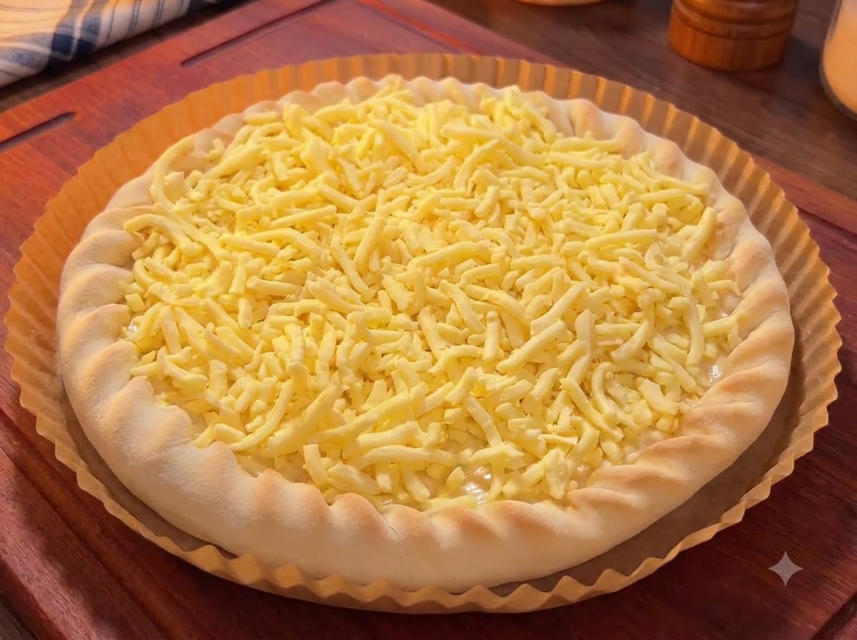 A pizza base covered with shredded cheese, topped with colorful pieces of mango, dragon fruit, and cherries.