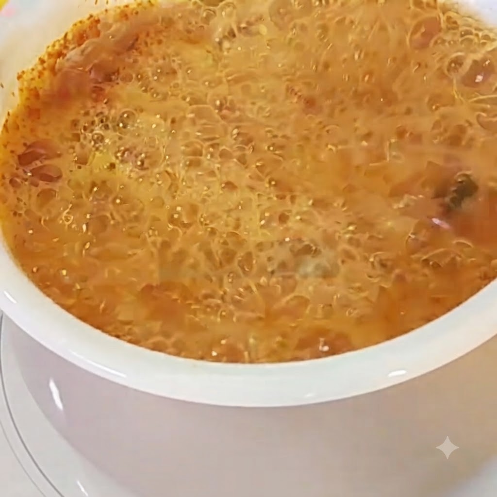 An egg cracked into a pot of bubbling red ramen broth.