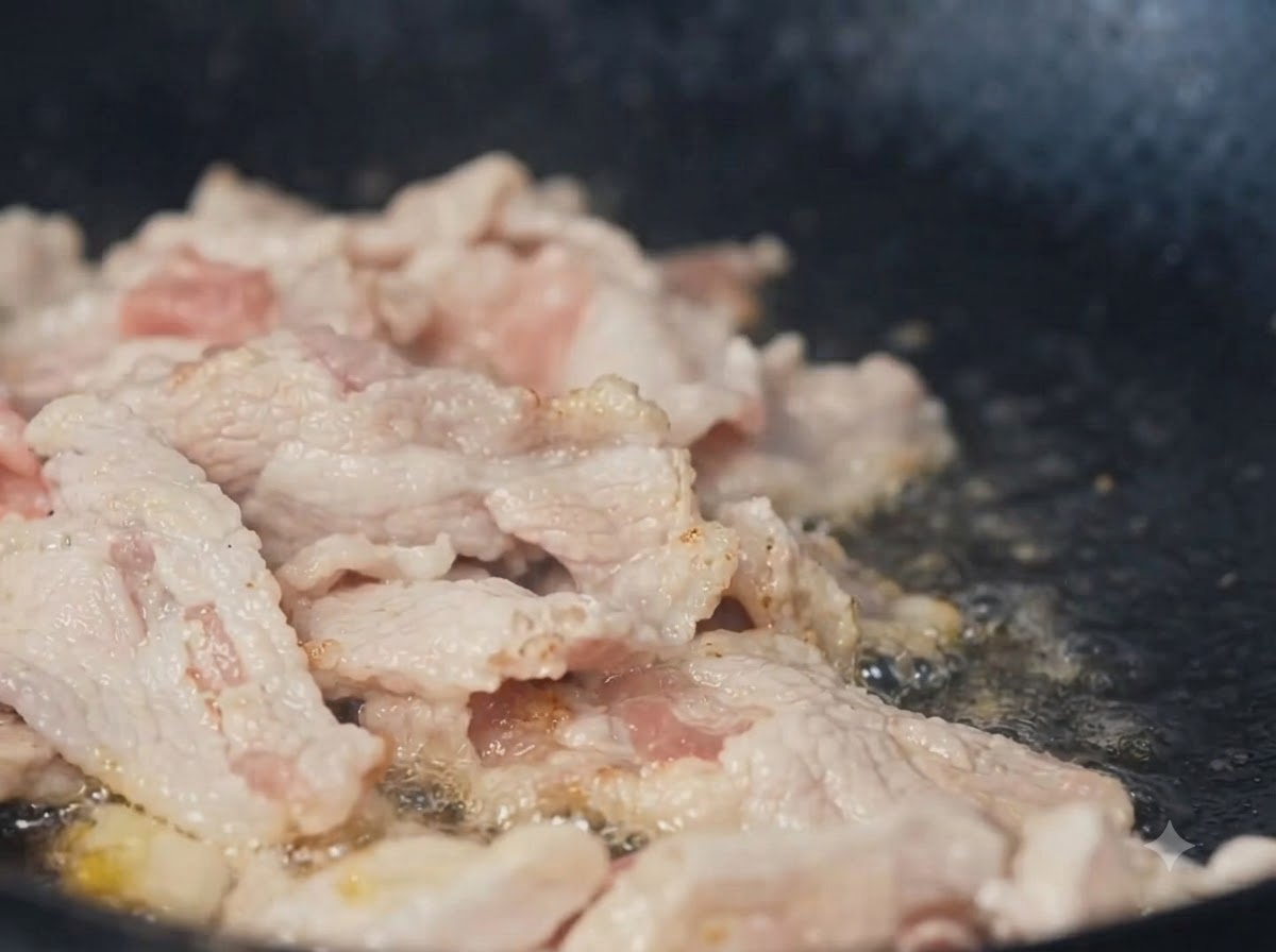 Sliced pork being stir-fried in a wok.