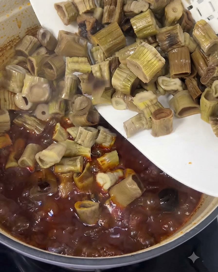 Chopped bamboo shoots sliding from a white plate into a bubbling red beef stew.