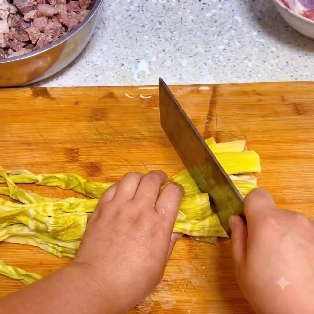 A kitchen knife cutting yellow rehydrated bamboo shoots on a wooden cutting board.