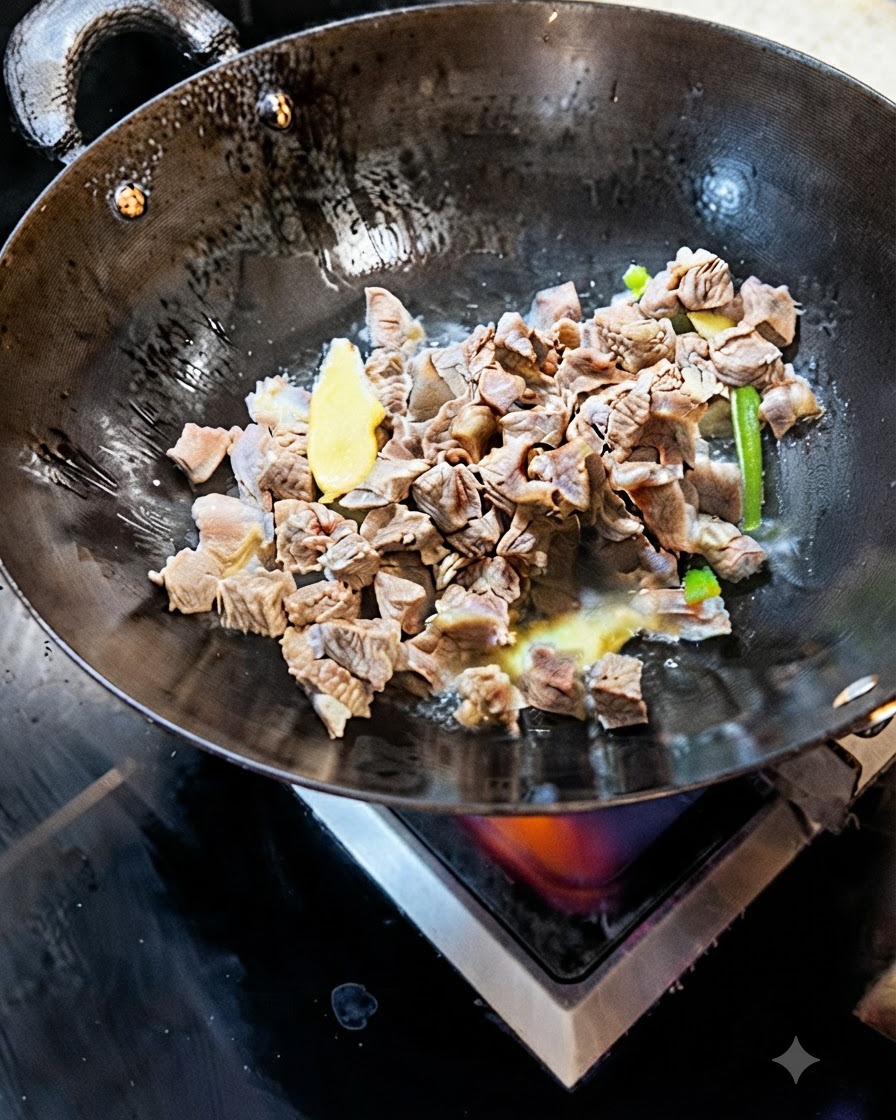 Blanched beef cubes stir-frying in a wok with slices of ginger and green onion.