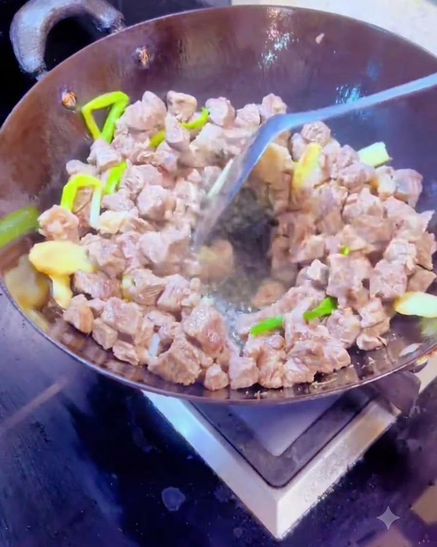 Stirring dry spices and beef cubes together in a hot wok using a metal spatula.