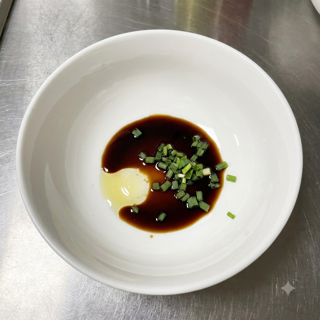 A white bowl containing light soy sauce, freshly chopped green scallions, and a dollop of seasoning paste on a stainless steel counter.