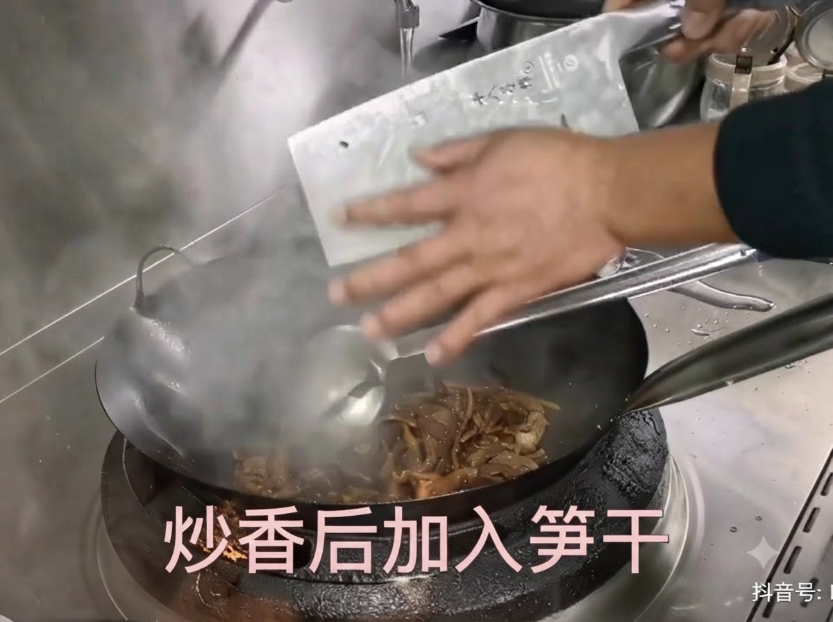 Prepared dried bamboo shoots being scraped from a cleaver into a hot wok with stir-frying pork.