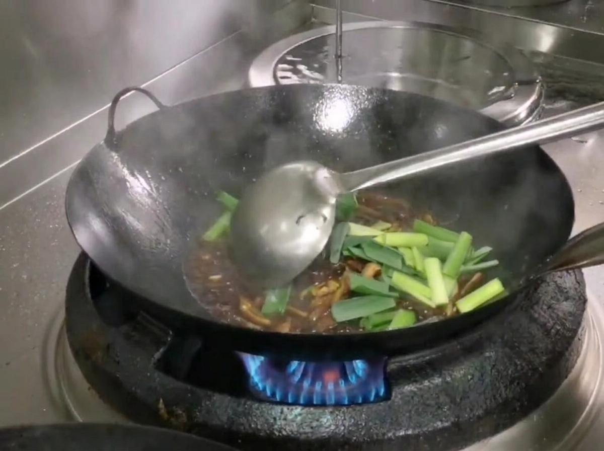 Fresh green garlic shoot sections added to the wok and mixed with the ingredients using a ladle.